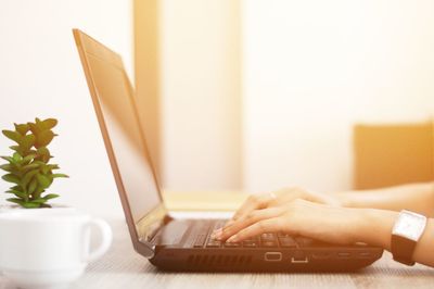 Cropped hands of woman using laptop at table