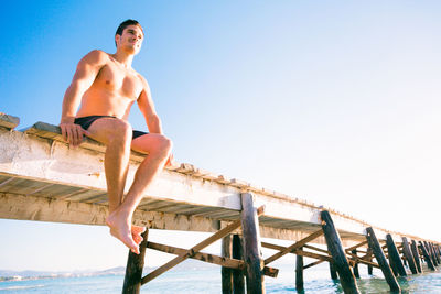 Low angle view of shirtless man on railing against clear sky