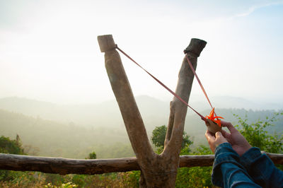 Cropped hands holding slingshot against mountains