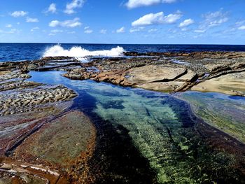 Scenic view of rock pools against sky and surf