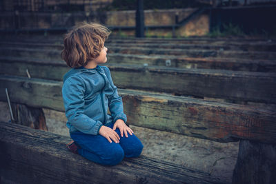 Side view of boy looking away while sitting on wood
