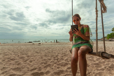 Man using mobile phone at beach against sky