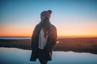 Woman standing on beach against sky during sunset