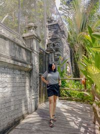 Full length of young woman looking away while standing against gate