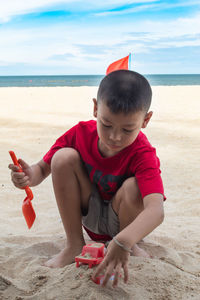 Boy crouching while playing with sand at beach