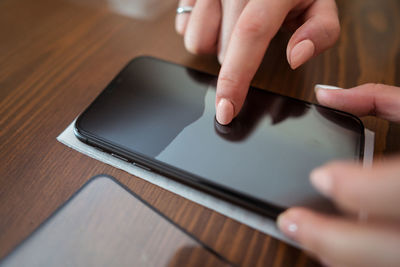 Soft focus of anonymous female attaching new protective glass to screen of mobile phone on table