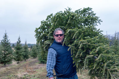 Portrait of mature man holding tree while standing on field