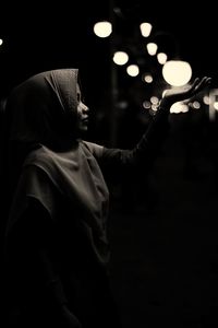Young woman holding illuminated light while standing outdoors at night