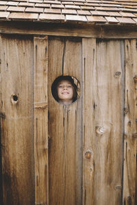 Portrait of playful boy seen though wooden wall's hole