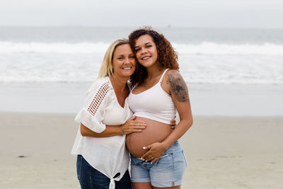 Mom posing with pregnant daughter on beach