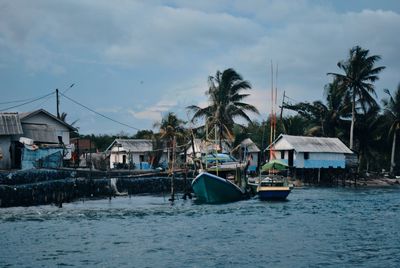 Sailboats in sea by houses against sky