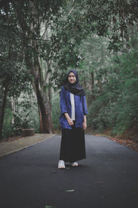 Girl standing on road amidst trees