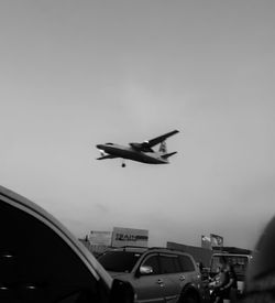 Airplane flying over road in city against sky