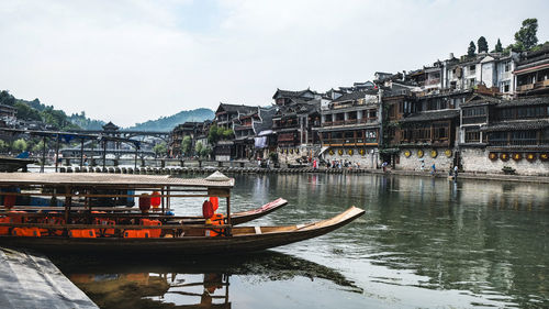 Boat moored on river by buildings against sky