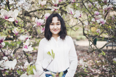 Cheerful asian young woman in a white blouse under the magnolia blooming tree