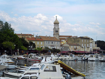 Boats moored at harbor against sky in city