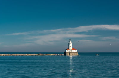 Lighthouse by sea against blue sky