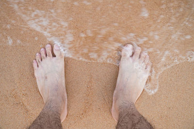 Low section of man standing on wet sand