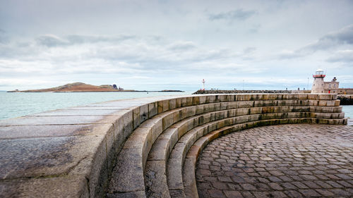 View of steps by sea against cloudy sky