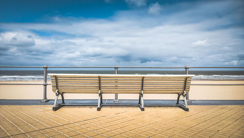 Empty bench on beach against sky