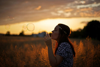 Young woman with umbrella against sunset sky