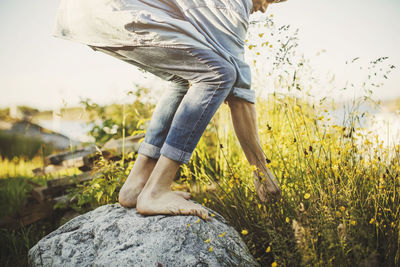 Low section of young man standing on rock by flowers