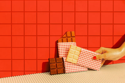 Woman hand putting chocolate bar against red tile wall