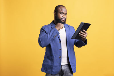 Portrait of young man using mobile phone against yellow background