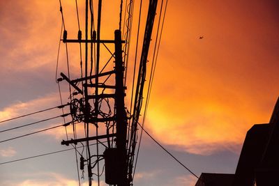 Low angle view of silhouette electric pole against orange sky