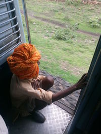 Man wearing orange turban while crouching on train doorway