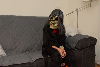 Portrait of woman wearing evil mask while sitting on sofa at home