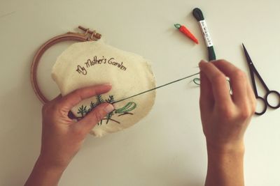 Cropped image of craftsperson doing embroidery on cloth over white background