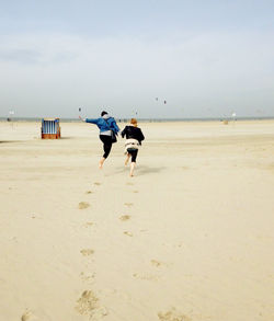 Rear view of women running on beach against cloudy sky