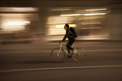 Side view of man riding bicycle on illuminated city