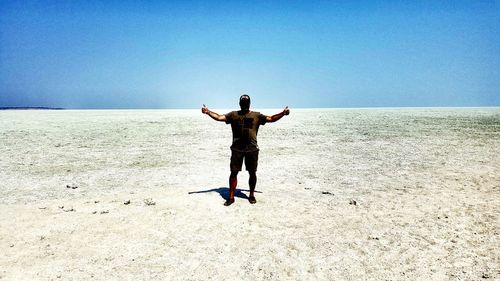 Rear view of man standing on beach against clear blue sky