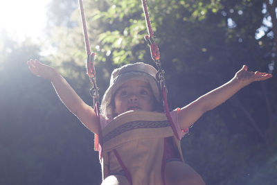 Low angle view of girl on swing against trees