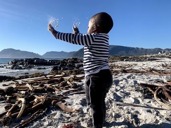 Rear view of boy standing on shore against sky