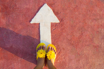 Low section of woman in yellow slippers standing on street with arrow symbol