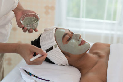 Midsection of beautician applying facial mask on smiling woman face at spa