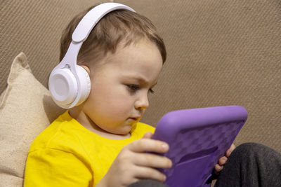 Little caucasian boy with yellow shirt playing game on digital tablet at home. 