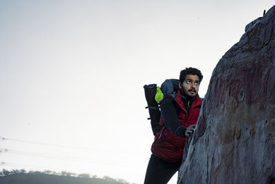 Young indian climber and traveler climbing up the mountain rock during sunset. adventure