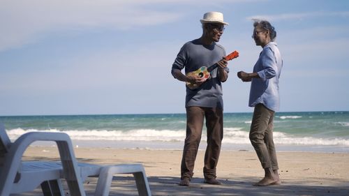 Happy senior couple relaxing outdoors singing and playing acoustic guitar at beach near sea sunny