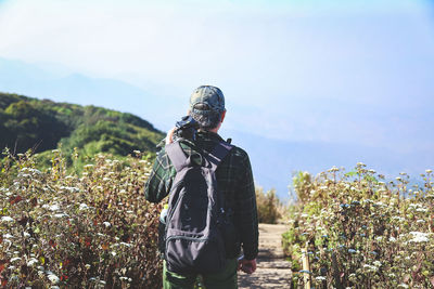 Rear view of man standing amidst plants against sky