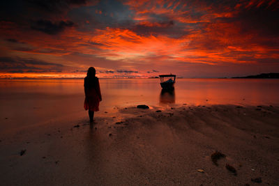 Silhouette woman standing at beach against orange sky