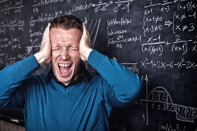 Frustrated man touching head in pain against formulas on blackboard