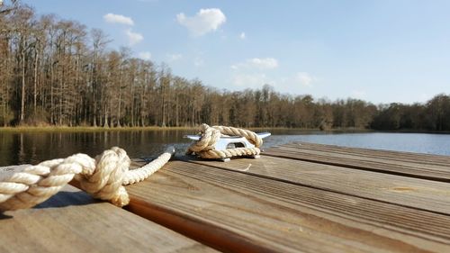Close-up of rope tied to bollard on pier in lake against sky