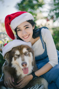 Portrait of smiling woman wearing santa hat with dog sitting outdoors