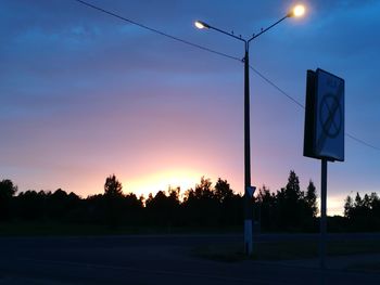 Road sign by silhouette trees against sky at sunset