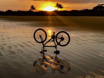 Silhouette bicycle by lake against sky during sunset