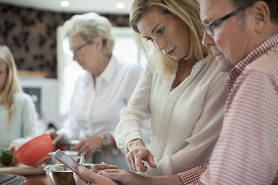 Woman using digital tablet with father-in-law while cooking in kitchen